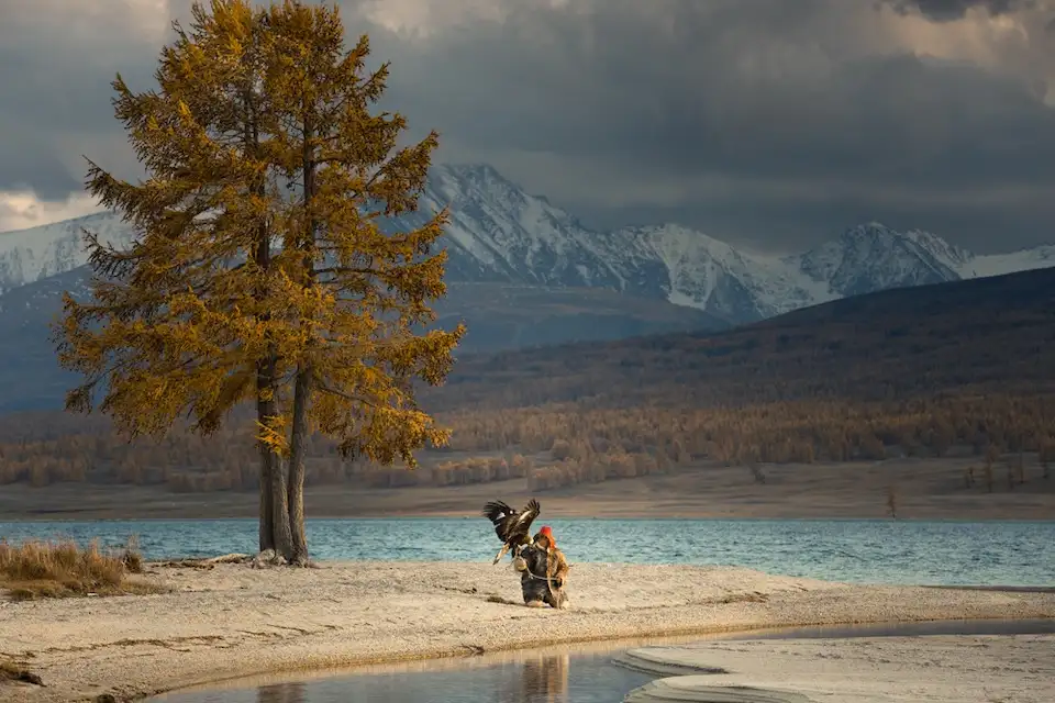An eagle hunter rests beside the heart-shaped lake, autumn colors and tradition in Mongolia's Altai