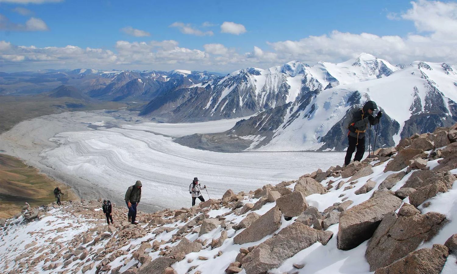 Trekkers climbing a rocky ridge above the vast Potanin glacier in Altai Tavan Bogd National Park