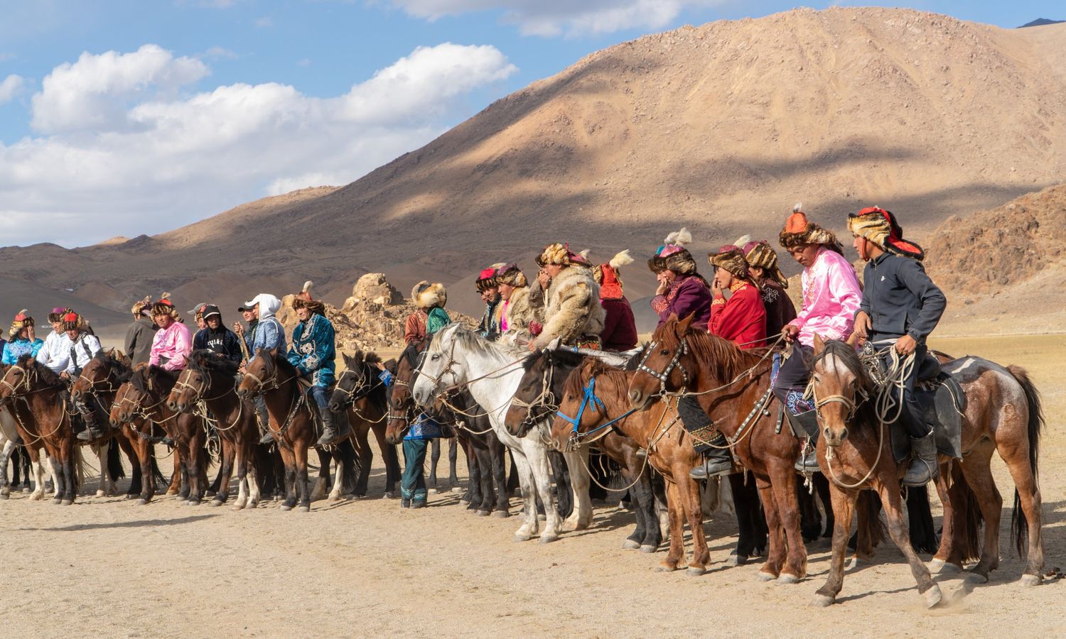 Eagle hunters in traditional dress lined up on horseback beneath the Altai mountains
