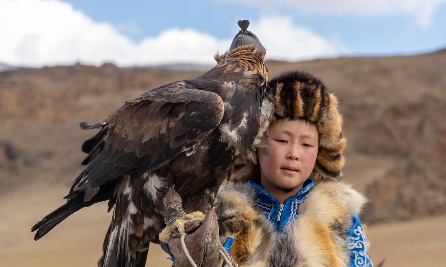 A young Kazakh eagle hunter in a fur hat holding his golden eagle